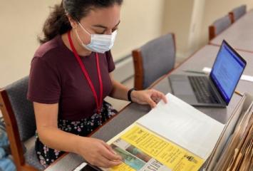 Person with long brown hair in a ponytail wearing a mask looking at a folder of JHC archival papers.