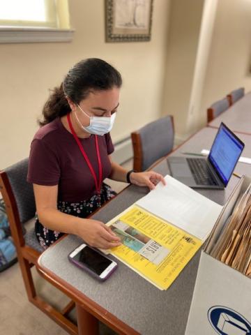 Person with long brown hair in a ponytail wearing a mask looking at a folder of JHC archival papers.